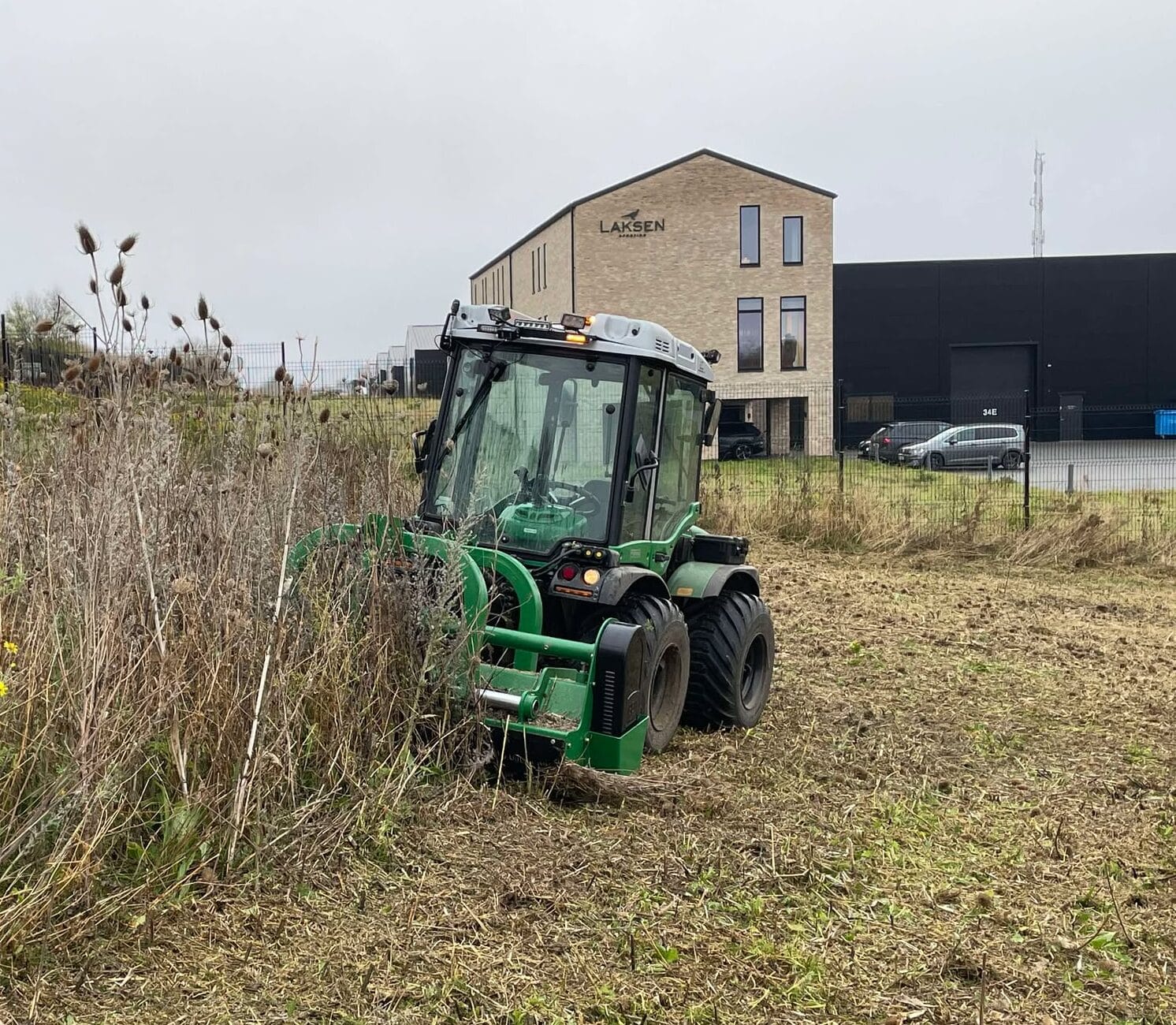 Traktor er i gang med Brakpudsning og klipper græs ved bygning